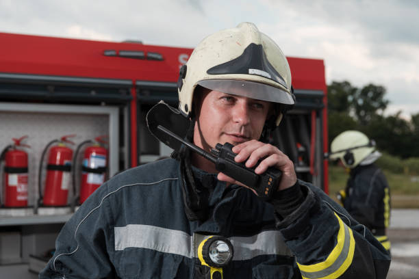 strażak używający walkie talkie w akcji ratowniczej, wóz strażacki i zespół strażacki w tle - sports uniform audio zdjęcia i obrazy z banku zdjęć