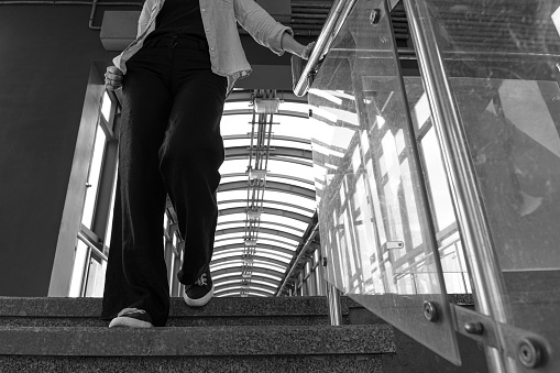 woman walking down the stairs holding onto the railing. a woman walks along an overpass. girl holding on to the railing. black and white photography