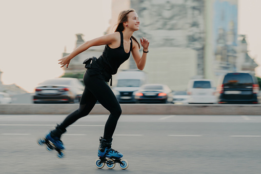 Young, slim woman enjoys fast-paced rollerblading, wearing black t-shirt and leggings. Active rest and sport training concept.