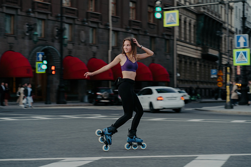Slim woman rollerblading outdoors, trains legs, core, and endurance, burns calories, improves balance in a cardio workout.