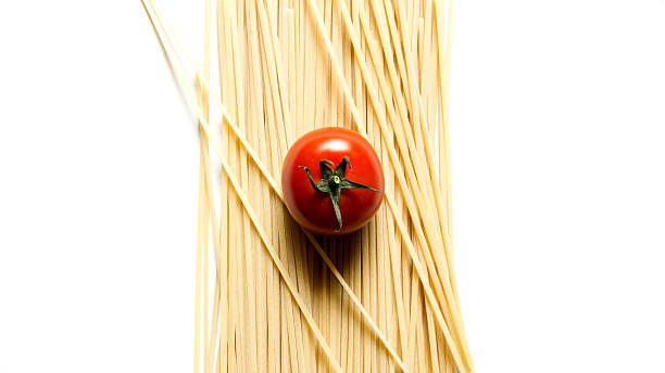 crudo pasta e un pomodoro fresco su sfondo bianco - teigwaren foto e immagini stock