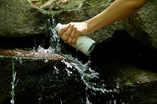 Girl fill water bottle by mountain spring during summer walk in nature