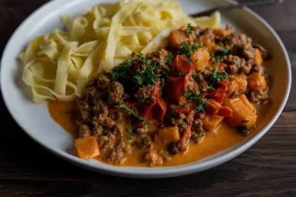 Delicious creamy pasta and beef dish with sweet potatoe, tomatoes, peppers in a cream sauce on a plate.