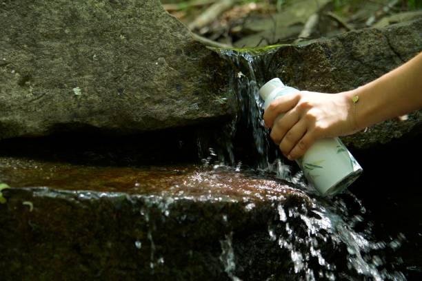 Girl fill water bottle by mountain spring during summer walk in nature