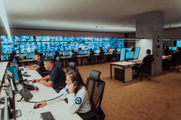 groupe d’opérateurs de centres de données de sécurité travaillant dans une salle de surveillance cctv regardant sur plusieurs moniteurs. les agents surveillent plusieurs écrans à la recherche d’activités suspectes - salle de contrôle photos et images de collection