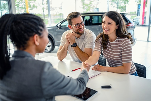Happy couple came to an agreement with a car salesperson at a meeting in a showroom.