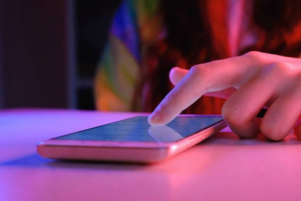 Use of mobile phone in trendy neon lights with laptop computer at night. Creative vivid color of ultraviolet red and blue. Hands of Girl scrolling up photos at smartphone Close-up at dark room. App for sale in shop, Social media. Female uses smartphone. Internet security, cyber attack. Trendy neon light. Creative vivid color of ultraviolet red and blue. 4K. pink and blue illumination. blog content. cyberspace, sale shop, delinquency concept. data theft, data protection. mobility. wifi. easy pay uso del teléfono móvil en luces de neón de moda con computadora portátil. color vivo creativo de rojo ultravioleta y azul. manos de chica desplazándose hacia arriba fotos primer plano en cuarto oscuro. app en venta en tienda, social media.