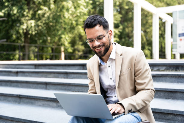 istock Handsome man working on laptop in city street. Man using his knowledge while sitting on stairs outdoors. Businessman successful finishing task project on computer in-front of office building 1504005750