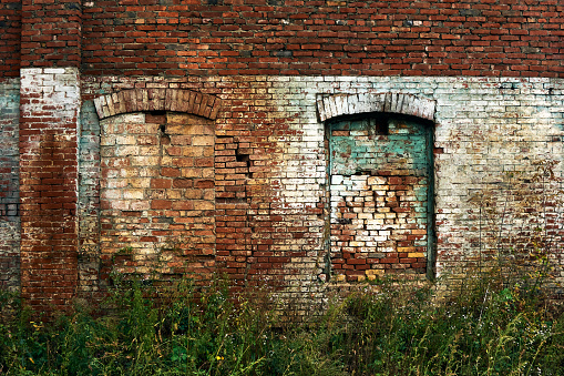 Wall of an old abandoned factory, old brick, painted in places, arched windows tightly bricked up, abandoned and unnecessary building