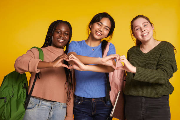 Ready for a new school year Three teenage girls embracing each other against yellow background heart hands multicultural women stock pictures, royalty-free photos & images