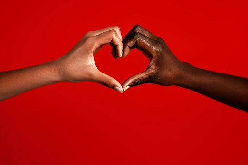 Two multiracial girls making heart sign against red background