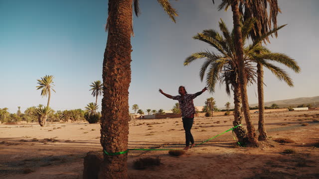 Man walking on tightrope between palm trees at beach in Morocco