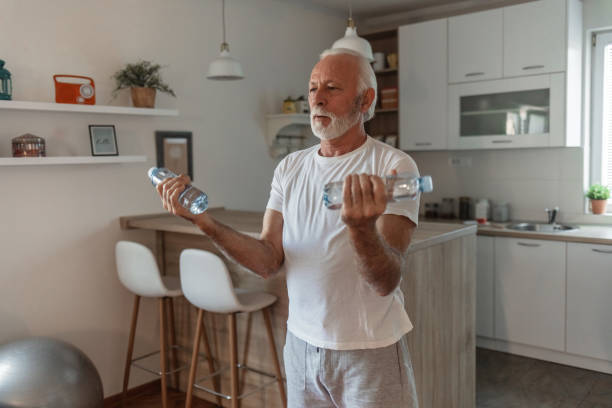 istock Healthy man exercising at home. Positive old man exercising at home, using water bottle weights. 1504040868