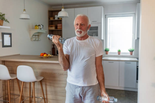 istock Healthy man exercising at home. Positive old man exercising at home, using water bottle weights. 1504040938