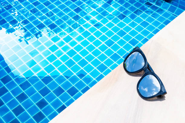 istock Sunglasses with sky reflection on swimming pool edge with space on blue water background 1504041449