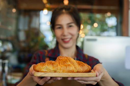 Close-up camera in front bakery owner handing out tray with small croissants, slowly backed away at reasonable distance, woman pulled tray back toward herself, It's small tray for eating in shop.
