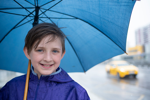 portrait of a smiling 10 year old boy under a blue umbrella on a rainy day