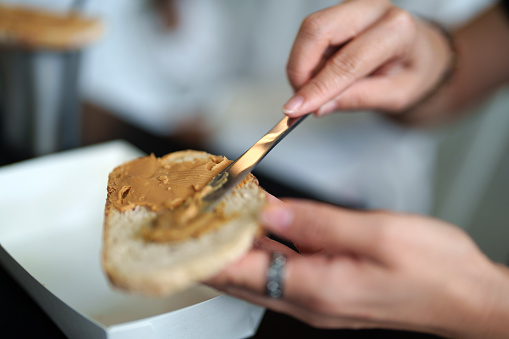 istock Close up woman spreading peanut butter cream over bread slice 1504080886