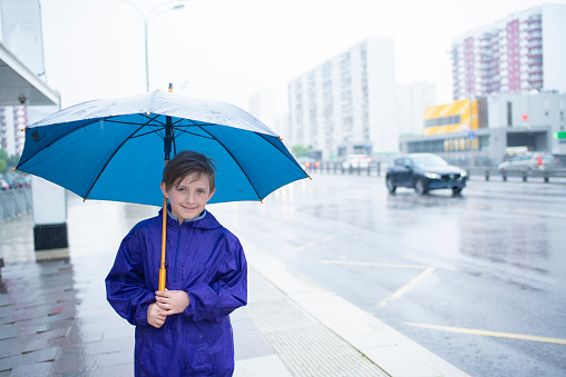 a smiling 10 year old boy under a blue umbrella on a rainy day
