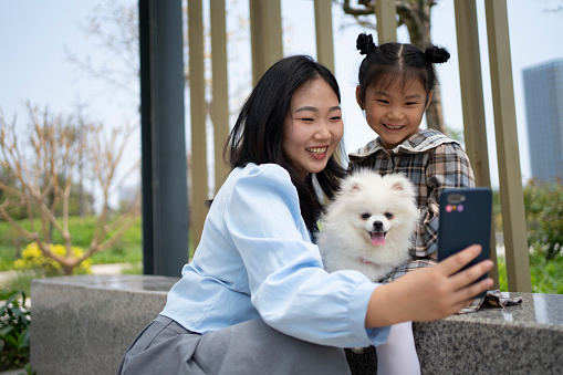 This young mother and her daughter are taking photos outdoors using their smartphones