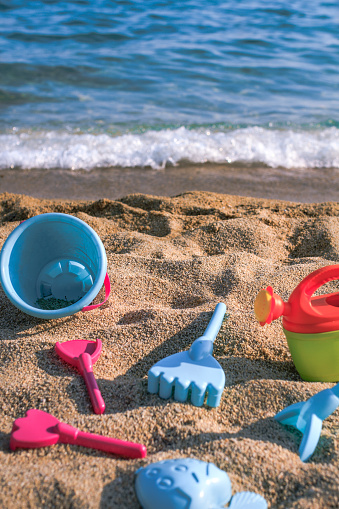 Colorful beach toys in the sand by blue sea. Sand pail and shovel, bucket, rake and prayers on the beach near the sea. Space for text
