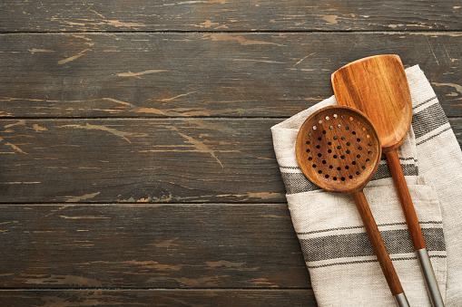 Cutting board with kitchen spoons and red napkin and parsley, tomato for cooking on old wooden dark background. Vegetarian food, health or cooking concept. Food background with free space for text.