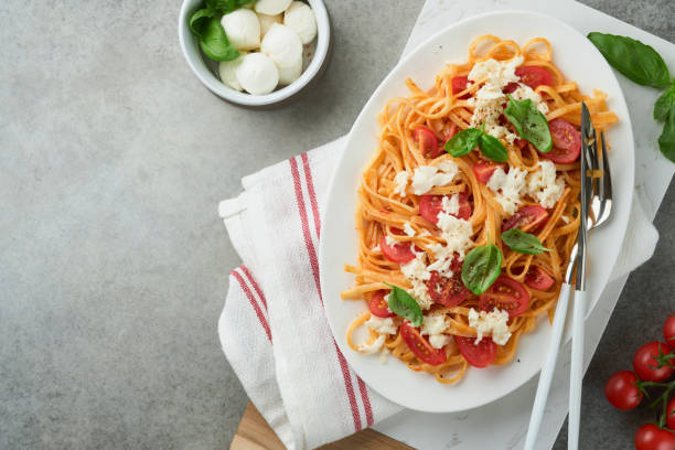 salat-caprese oder pasta-spaghetti gebrochen mit basilikum und mozzarella ala caprese auf weißem teller auf grauem rustikalem betonhintergrund. traditionelle italienische küche. italienisches food-konzept.  draufsicht. rezept. - caprese salad antipasto wine mozzarella stock-fotos und bilder