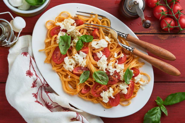 salat-caprese oder pasta-spaghetti gebrochen mit basilikum und mozzarella ala caprese auf einem weißen teller auf rotem rustikalem holzhintergrund. traditionelle italienische küche. italienisches food-konzept. draufsicht. - caprese salad antipasto wine mozzarella stock-fotos und bilder