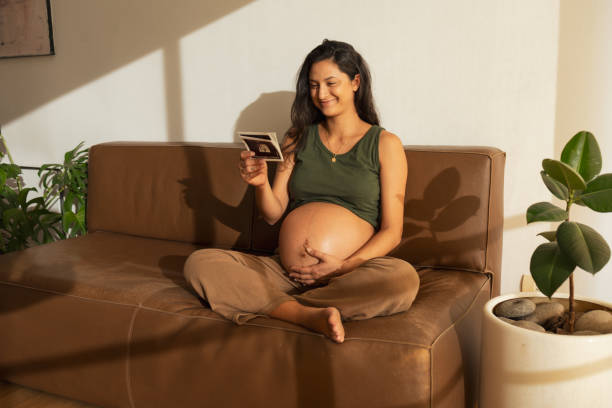 Happy pregnant woman looking at ultrasound scan at home stock photo