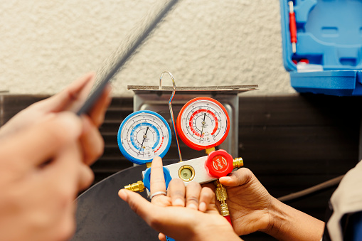 Close up of seasoned wireman holding pressure measurement device used for checking air conditioner refrigerant tank in need of repairing. Proficient expert using manometers to check freon levels