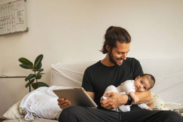 아버지는 온라인으로 일하는 동안 아기를 팔에 안고 있습니다 - 성혼합 뉴스 사진 이미지