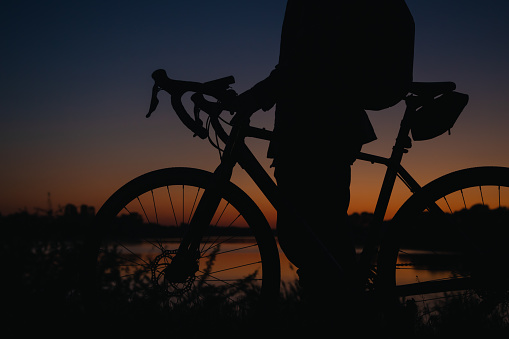 Silhouette of a man with a bicycle near the lake at sunset, the concept of sports and travel.