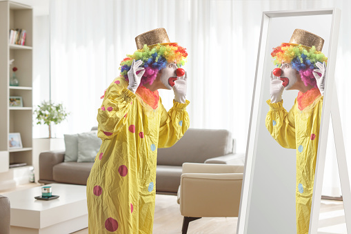 Clown in a yellow costume standing in front of a mirror in a living room
