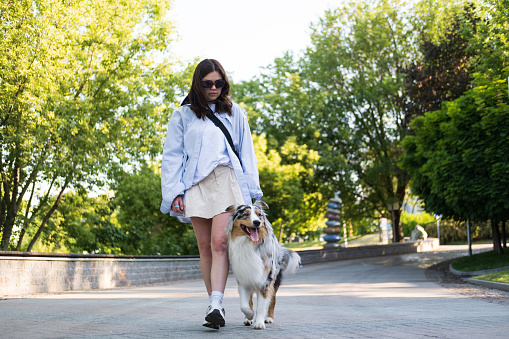 Young woman walking her aussie dog in an urban alley, spending time with pets outdoors. Mid 20s girl with australian shepherd dog on the leash
