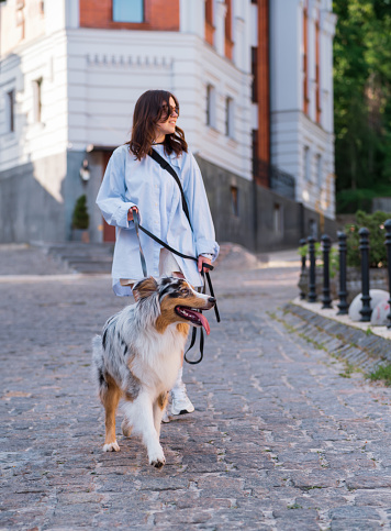 Young woman and her asutralian shepherd dog on the leash, selective focus on the dog. Walking with pets downtown in the city, lifestyle image