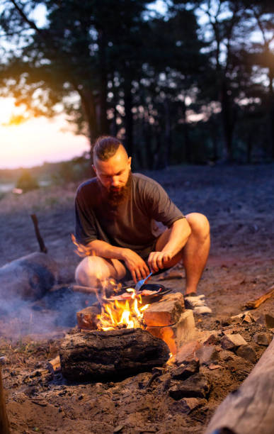 istock A young man with a beard prepares a dish of bacon with scrambled eggs on a fire. Cooking and outdoor recreation in summer. 1504169704
