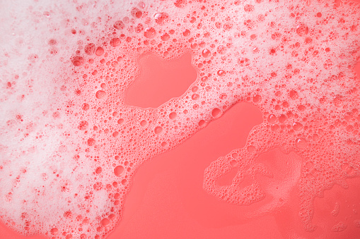 Texture of white foam with bubbles on pink background. Cosmetic foam for washing, hygiene, shampoo, soap, bathing gel, mousse. minimalistic cosmetic and medical background flat lay