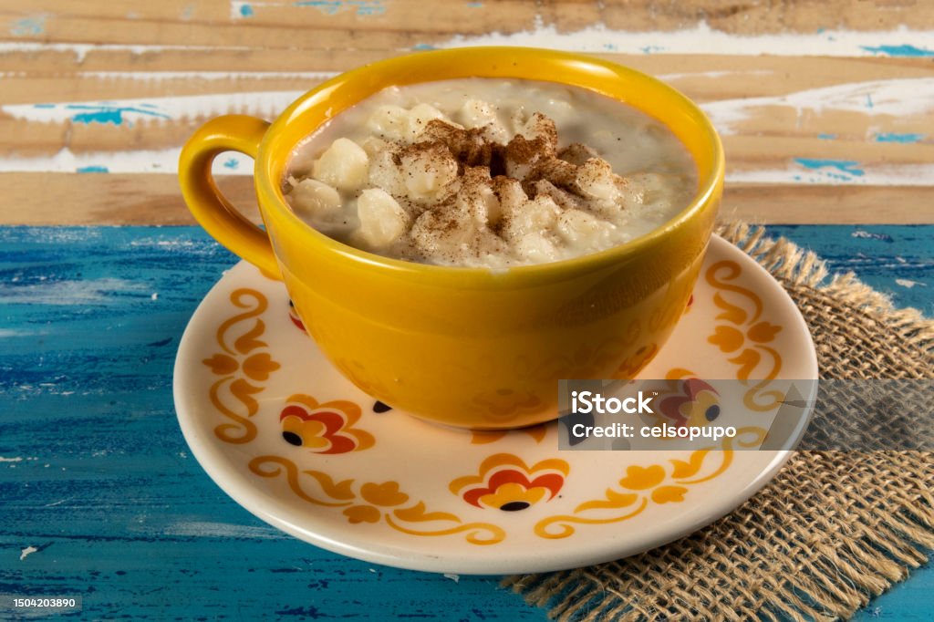 cup of canjica, typical food consumed in the Brazilian Festa Juninas Typical Brazilian sweet dessert, Canjica. White corn porridge with cinnamon and coconut. Consumed at June festivals (festa Junina) on a rustic blue table Porridge Stock Photo