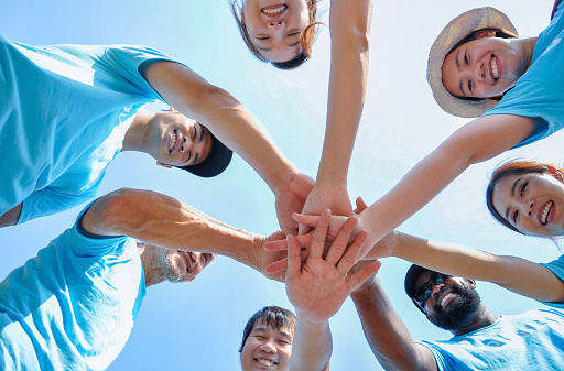 low angle,group of happy diversity people smile,stacking hands to support,trust,help,success for commitment voluntary charity while working outdoors