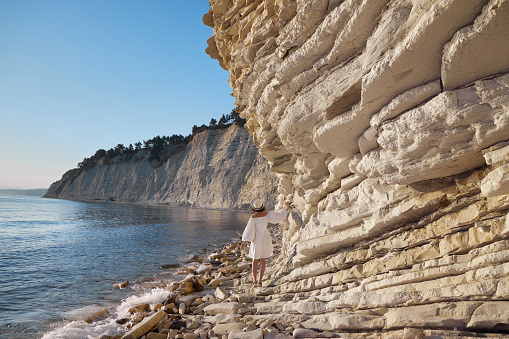woman in white dress walking near shore on cliff edge