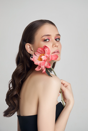 Beauty Woman with big pink flowers, studio portrait. Perfect body, pink professional makeup on a woman face. Curly hair