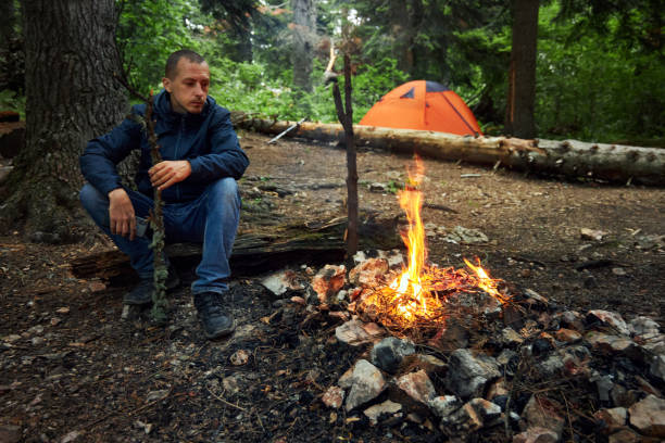 istock man sitting by a fire while camping in the woods 1504221817