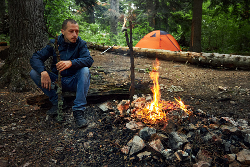 man sitting by a fire while camping in the woods