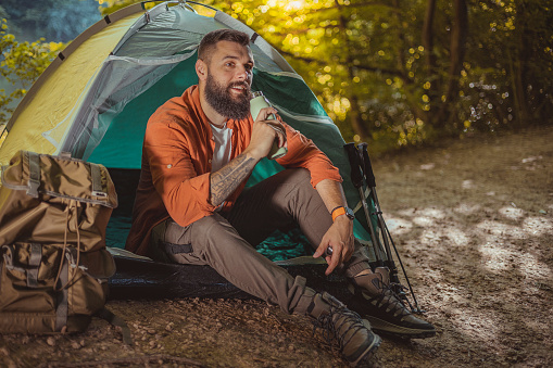 Handsome Bearded Young Man Holding a Thermos While Relaxing Near Tent During a Hike