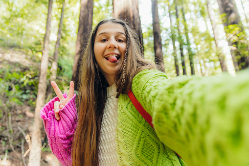 Self portrait of smiling female with long hair wearing colourful sweater making tongue-out in scenic forest with redwood trees in Monterey Peninsula, the USA