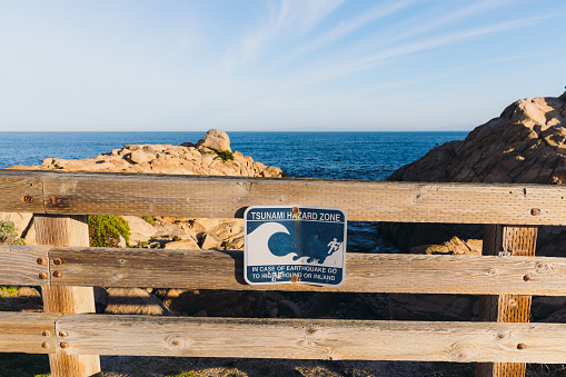 A view of the sign of attention of high risk of tsunami at the rocky coastline of 17-Mile Drive in the United States