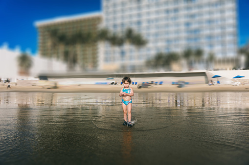 3 year old, multiracial girl wades curiously in the shallow ocean tide during a sunny, summer vacation at a resort.