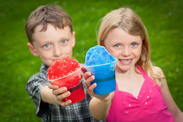 Photo of Two kids hold snow cones out to the camera.