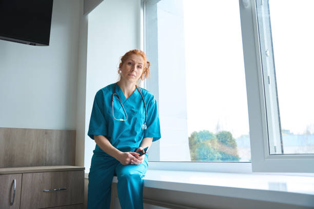 Female doctor sitting on the windowsill in hospital stock photo