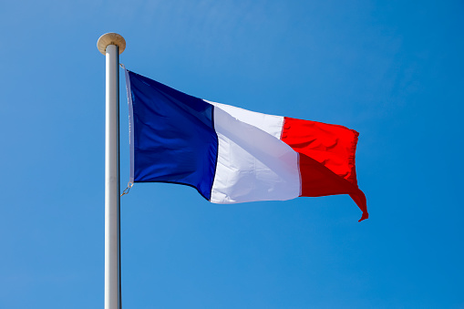 The national Flag of France is positioned on top of the mast and there it waves in the wind and is visible in the blue sky in Nice, France.